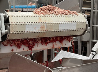 Ground beef traveling over the end of the conveyor belt, sticking and falling to floor